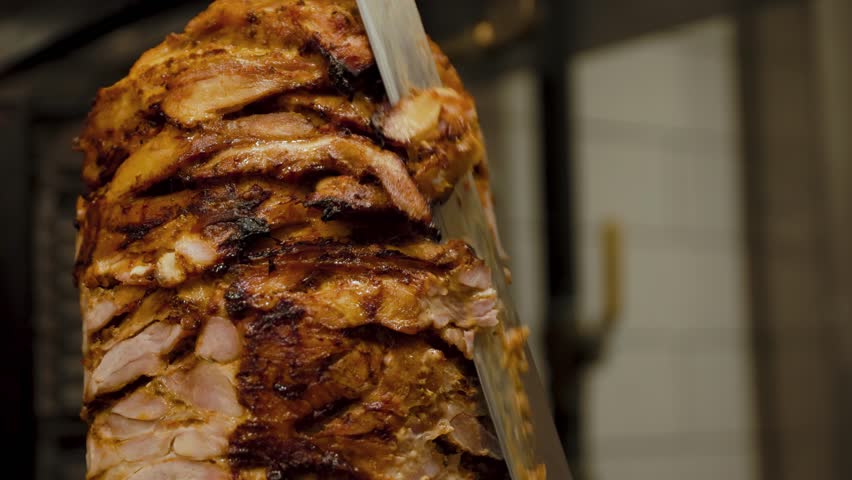 Close-up of a chef slicing meat off a rotating doner kebab, perfect for street food, restaurant, and culinary preparation visuals.