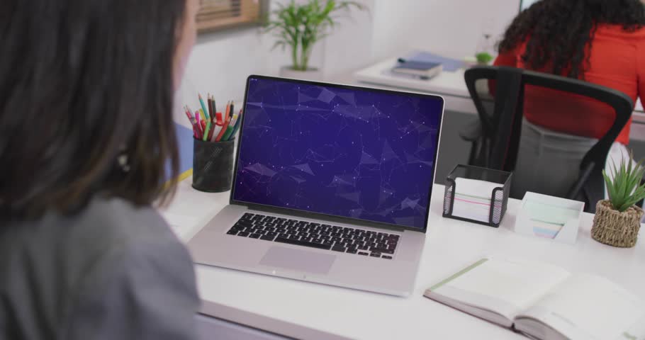 Woman leaning toward laptop and activating NFT graphic, expanding global map overlay across desk. Technology, digital, innovation, workspace, business, teamwork, modern