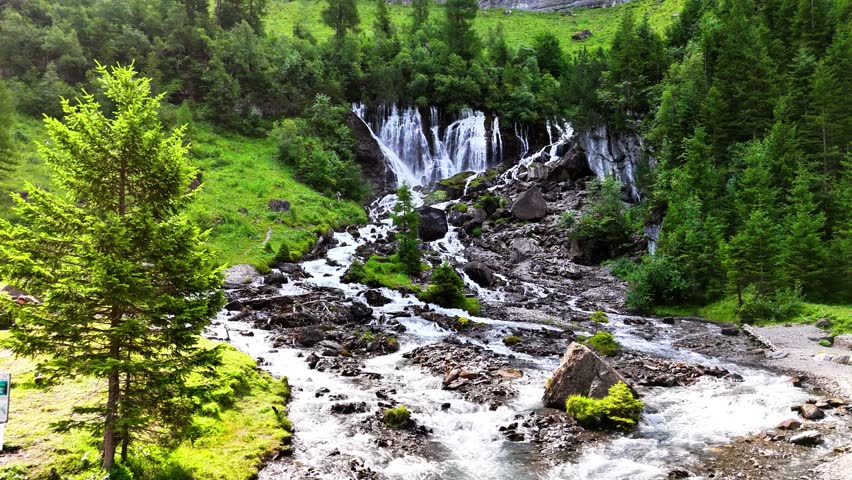 Waterfall at Lenk, Sibenfälle in Switzerland with cascading streams flowing through rocks, surrounded by green forest, alpine trees, and bright moss-covered terrain in a mountain valley environment