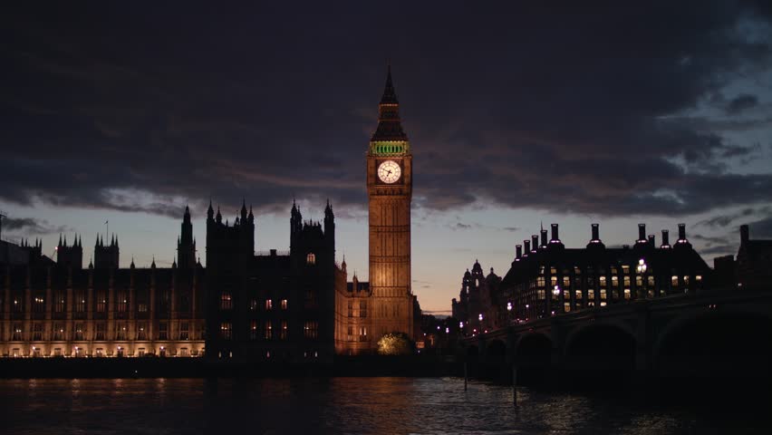 Westminster’s iconic Big Ben tower shines with golden lights beside the illuminated Houses of Parliament and bridge, their reflections shimmering on the River Thames after dark