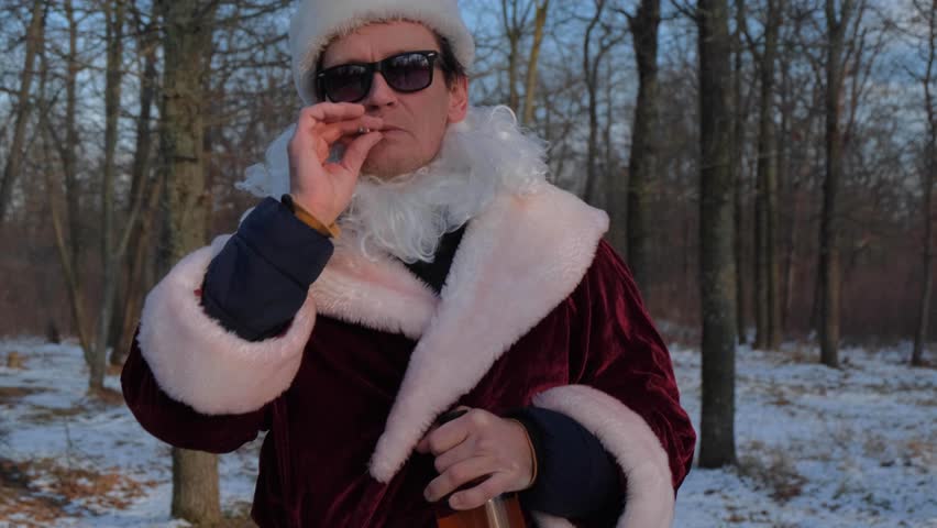 A man dressed as Santa Claus staggers through a winter forest, smoking a cigarette, and trips.
