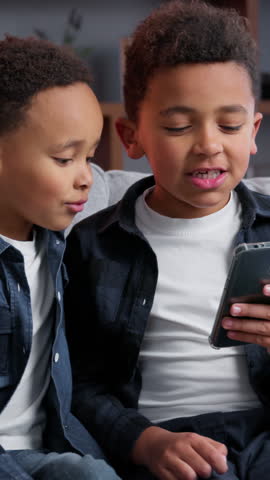 Two little African American boys looking in mobile phone using smartphone gadget addict generation siblings family boys children kids brothers playing internet game scrolling at home overuse apps