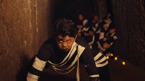 A dramatic male performer with intense makeup stares directly at the camera in a crawling pose, leading a group of dancers through a dark, candle-lit tunnel in a creepy, ritualistic scene. - Powered by Shutterstock - Get 15% off with code: PIKWIZARD15