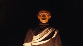 A man with dramatic spider makeup and white contacts is illuminated by a single light in the dark. He stares with a shocked expression as he slowly moves toward the camera. - Powered by Shutterstock - Get 15% off with code: PIKWIZARD15