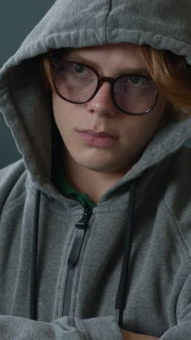 Vertical shot of depressed gen Z Caucasian guy covering face with hood being supported by unrecognizable people comforting him during group therapy session