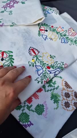 Real footage of a woman's hands examining antique embroidered tablecloths. Daylight, social media dimensions.
