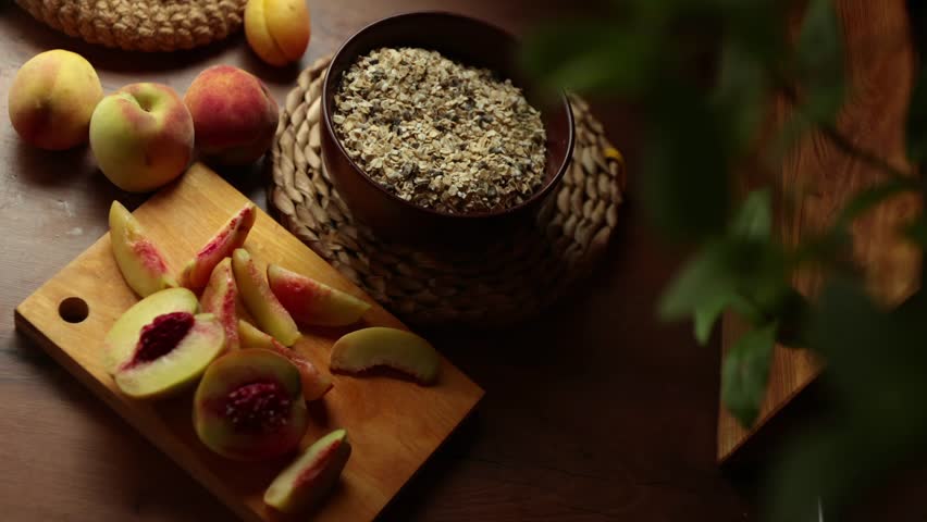 Freshly sliced peaches on a wooden cutting board next to whole peaches and a bowl of oats. Natural light enhances the warm colors of the scene.