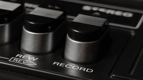 Macro shot of a finger pressing the record button on a vintage cassette tape deck, showing the textured black and silver key and adjacent rewind button with white text on an analog audio player. - Powered by Shutterstock - Get 15% off with code: PIKWIZARD15