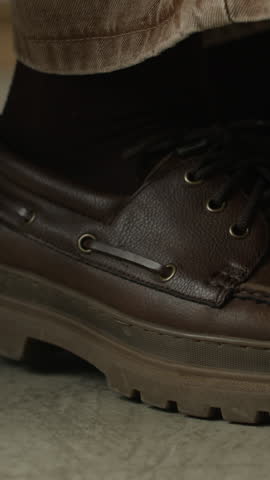 Vertical cropped close up shot of legs in brown shoes of unrecognizable person shaking because of anxiety or neurological disease