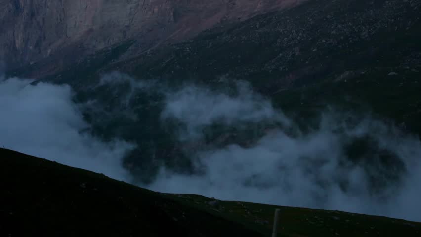Misty valley surrounded by mountains at dusk. Low clouds drift through the landscape, creating a serene and tranquil atmosphere.