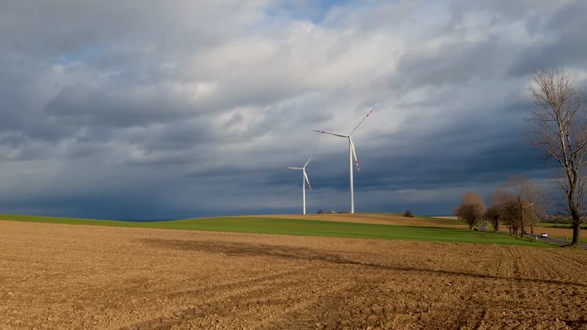 Large wind turbines stands tall in farm field under cloudy sky 