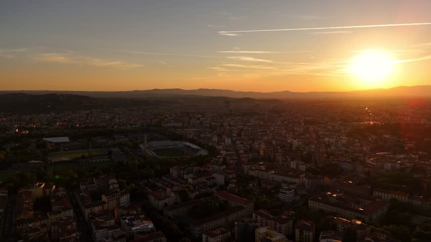 Cinematic drone sunset view over Florence rooftops, golden hour light casting warm glow on red terracotta roofs, panoramic urban landscape, aerial perspective, Italy cityscape