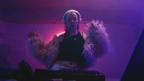 Woman DJ dancing in night neon party. Female disk jockey playing electronic music on techno rave, wear fur coat. Young girl jumping on set or stage, club mixer controller. Artist make modern sound - Powered by Shutterstock - Get 15% off with code: PIKWIZARD15