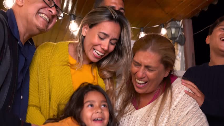 Hapy latin family smiling on camera during night time - Grandparents, parents and children - Multi generational people