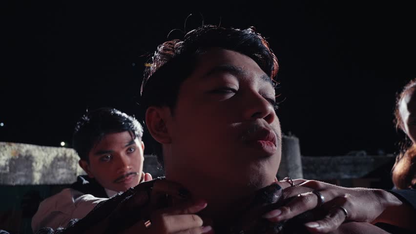 An intense close-up of a man's face being gently touched and held by the hands of his followers. A mysterious and intimate scene suggesting a cult, adoration, or a strange ceremony at night.