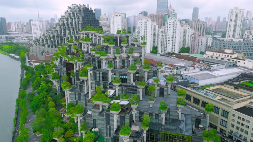 Aerial of the '1000 Trees' building, a terraced architecture with green trees and vegetation, situated by a river in Shanghai, China.
