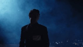 An artist or performer stands in silhouette on a rooftop or stage, surrounded by blue smoke. In the background, blurred city lights (bokeh) add to the cinematic and dramatic atmosphere of the night - Powered by Shutterstock - Get 15% off with code: PIKWIZARD15