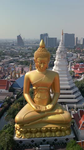 Aerial view of giant golden Buddha statue with white stupa and red temple roofs in Bangkok, Thailand. Traditional Buddhist architecture set against the modern city skyline.