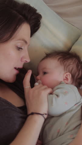 New Mum Cradling her Baby and Smiling in Bed at Home