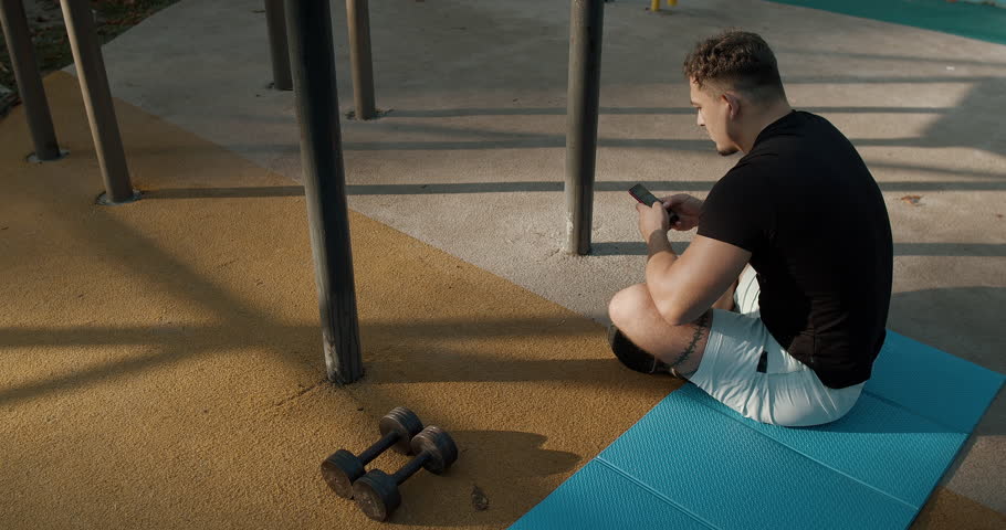 A Young Man Engaged in a Workout Session at an Outdoor Gym Utilizing Dumbbells for Exercise