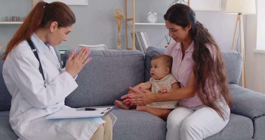 Female family doctor pediatrician with stethoscope begins homecare consultation and checkup, greeting a baby with mother on sofa at home ready for visit. Caring home checkup and medicine