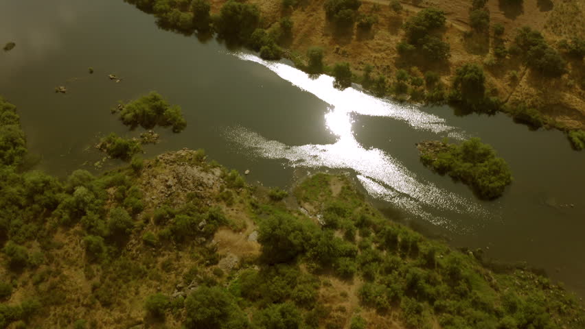 drone flying over a river with fields and trees on hills 
