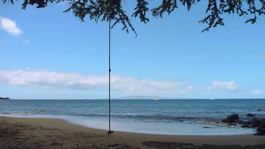 Model released man plays on rope swing, enjoying the beach and ocean in Hawaii,