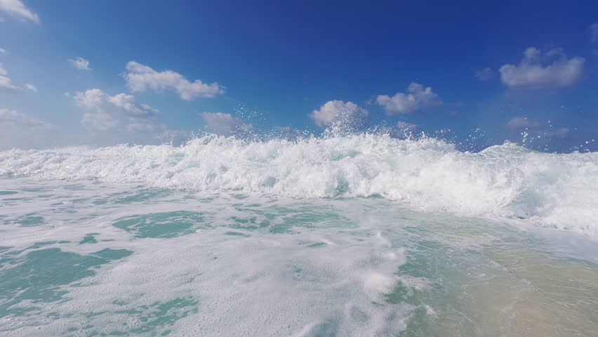 Slo-mo handheld PPV footage of rushing sea wave breaks over action camera. First POV of splashing waves