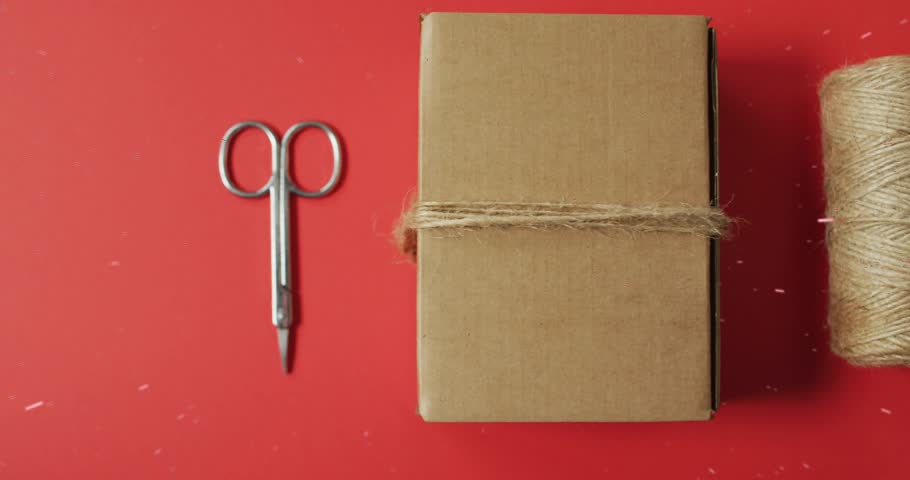 Flat-lay featuring spool sliding toward box starting gift tag entering and sprig completing wrap. Crafting, packaging, decoration, handmade, seasonal, rustic, minimalist