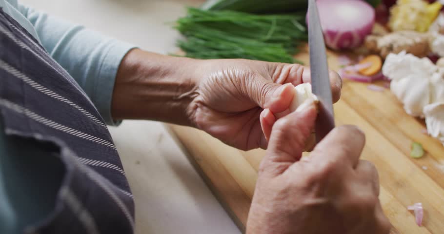 senior woman peeling garlic on wood top for cooking, rotating causing glitch overlay then slicing. Cooking, culinary, food preparation, kitchenware, traditional, digital disruption, asian cuisine