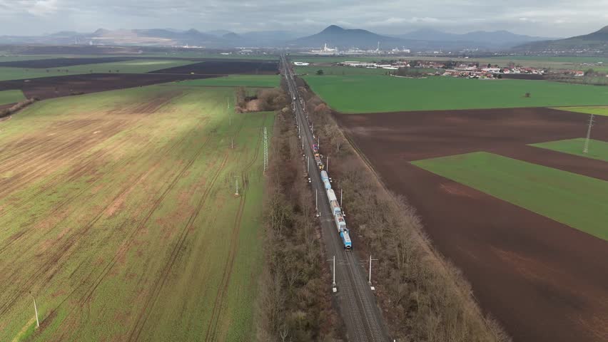 Aerial drone view of train moving along railway tracks into distance toward mountains, symbolizing travel, journey, landscape exploration, and scenic transportation.