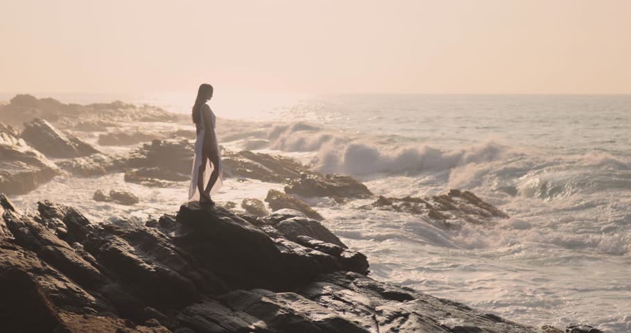 An epic cinematic shot of a woman standing on a cliffside by the ocean at sunset in Sri Lanka, highlighting the breathtaking scenery. Ideal for travel, adventure, and fashion-themed high-quality