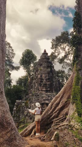 Female tourist in hat and shorts holding a map while exploring Victory Gate, Bayon Temple, Angkor Thom, Cambodia. High quality travel lifestyle stock footage for tourism promo and adventure campaigns.