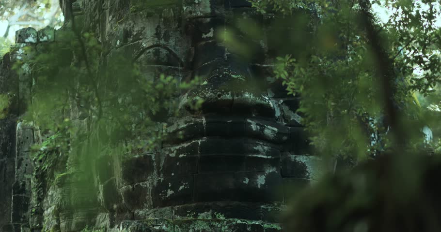 Close-up cinematic shot of the Bayon temple stone face partly hidden by jungle leaves at Angkor Wat, Cambodia. A mysterious and spiritual scene perfect for history, culture and fantasy concepts.