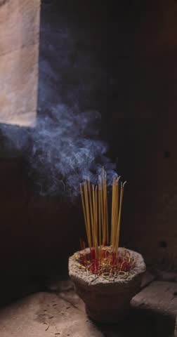 Slow motion footage of incense sticks burning in a clay pot with smoke gently rising in an ancient temple. Perfect for meditation, spirituality, culture, and creative promo video projects.