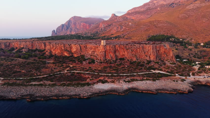 Coastal view of Sicily cliffs at sunset with calm sea and rugged terrain