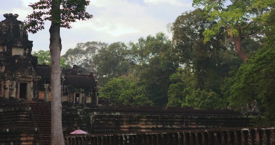 Camera pans sideways revealing the ancient Baphuon Temple partly hidden by trees in Angkor Archaeological Park, Cambodia. High quality conceptual footage for travel ads, history documentaries, or
