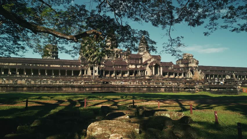 Aerial drone flies past trees and leaves heading directly towards the majestic Angkor Wat Temple in Cambodia. High quality cinematic footage perfect for tourism promos, documentaries, and epic travel