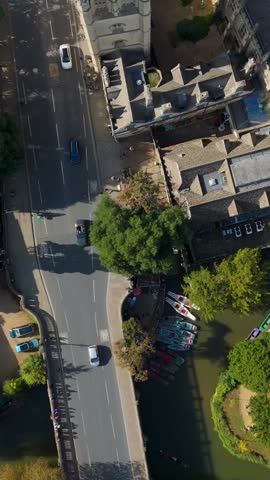 Vertical Aerial top-down drone shot of Magdalen College, Oxford. The flight moves diagonally over the Gothic tower, main building, and green courtyard, with dramatic long shadows.