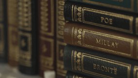 Extreme closeup sliding right shot on a macro lens of gold leaf leather bound books on a shelf with author names Poe, Millay, Brontë, and Plath embossed on the spines. - Powered by Shutterstock - Get 15% off with code: PIKWIZARD15