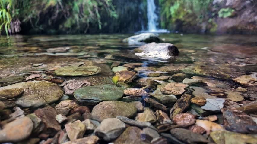 Clear water slowly flows over river rocks and pebbles from a distant waterfall