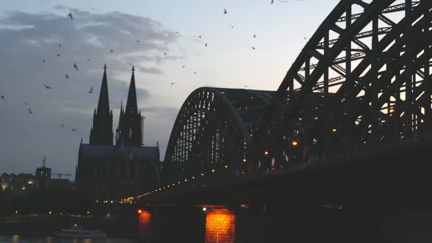 Cologne cathedral and hohenzollern bridge stand silhouetted against the evening sky