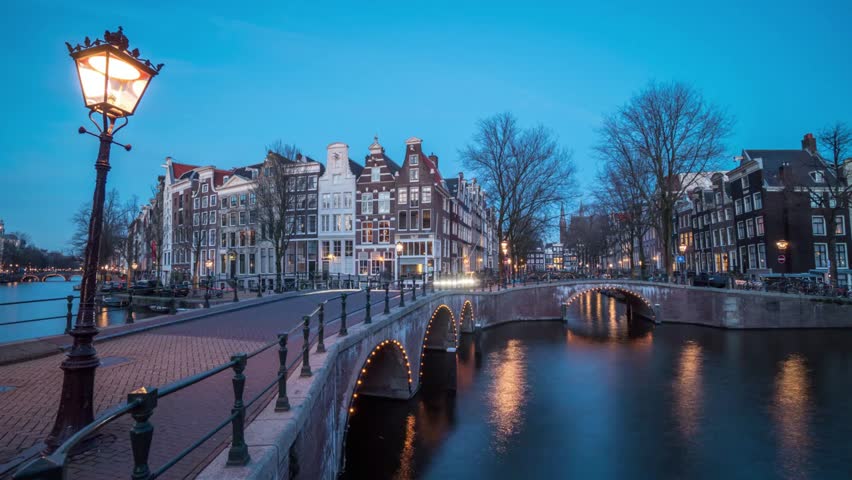 Illuminated street lamp shines on a bridge in amsterdam at twilight