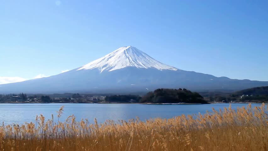 Mount fuji rises majestically over a tranquil lake under a clear blue sky