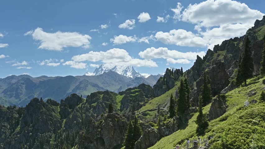 A scenic view of rocky mountains and green hills under a cloudy blue sky