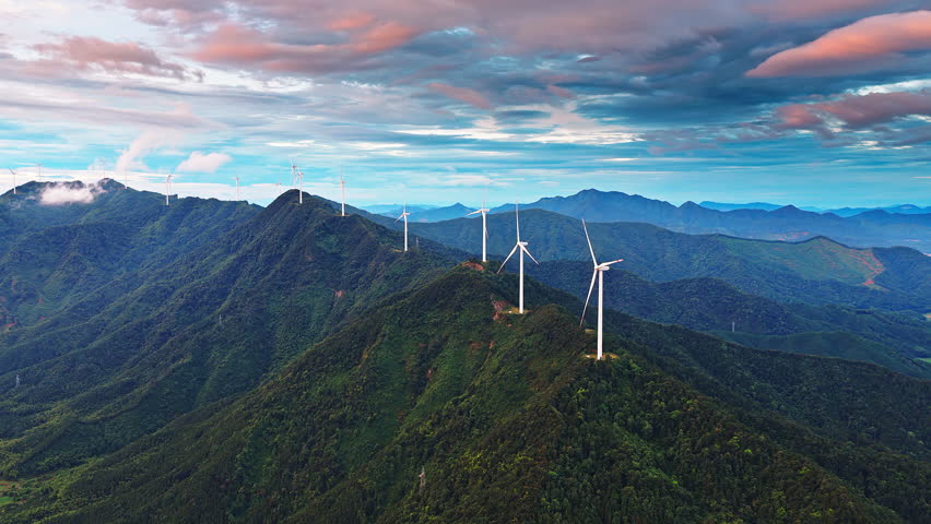 Aerial shot of wind turbines on green mountain ridge generating clean renewable energy under a beautiful dramatic sky