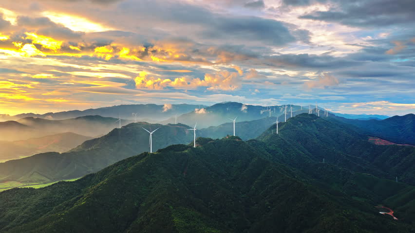 Aerial shot of wind turbines on a green mountain range generating clean renewable energy at sunrise