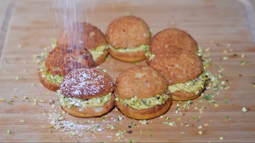 Close-up of cream puffs sprinkled with powdered sugar on a wooden table, delicious dessert in 4K.
