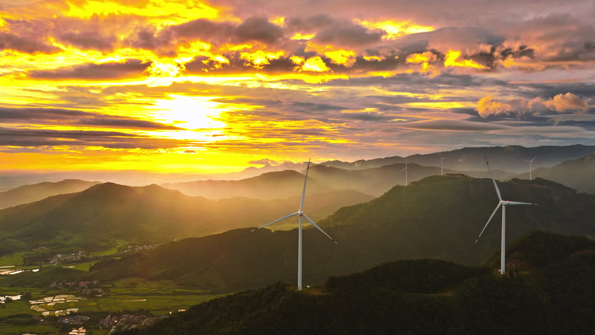 Aerial shot of wind turbines on a green mountain generating clean renewable energy with spectacular golden sunrise and dramatic sky