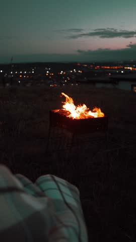 Enjoying a cozy evening by the fire on a hilltop with city lights in the background